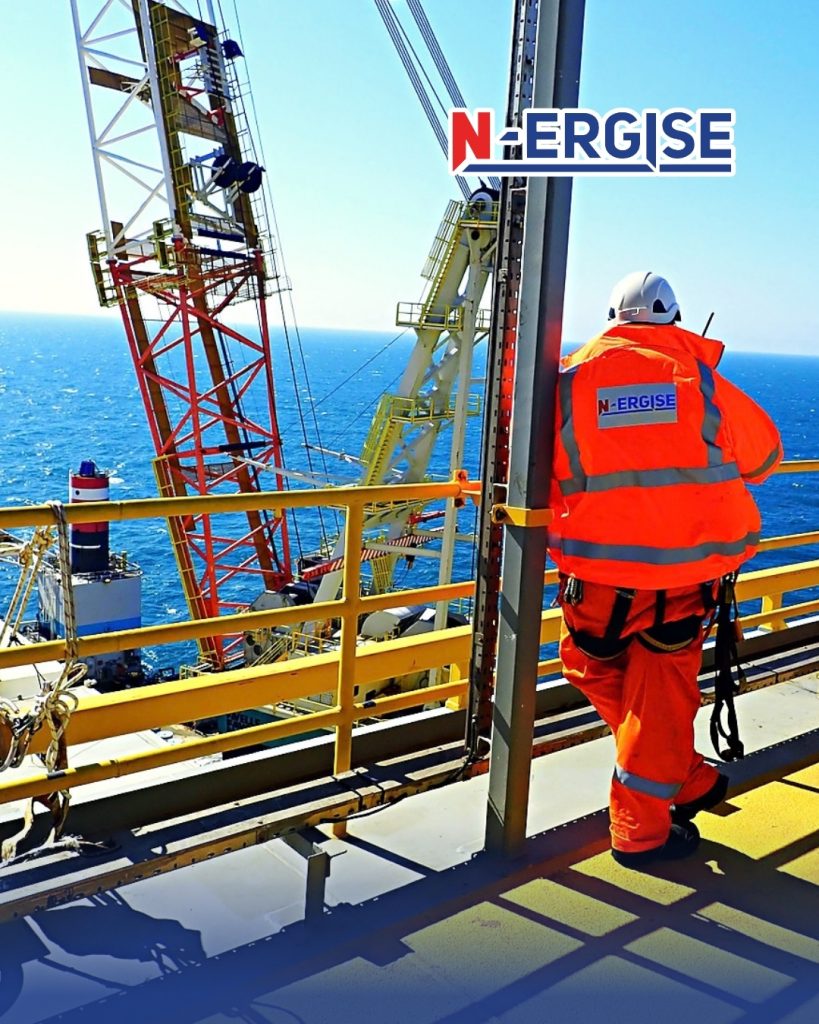 N-ERGISE Offshore worker in orange coveralls and a white hard hat looking out to sea from a platform deck beside a crane