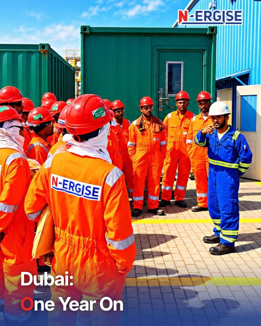 N-ERGISE Dubai team in orange coveralls and red hard hats at a safety briefing outside site cabins, led by a supervisor in blue coveralls, with the headline Dubai: One Year On (AI-generated image)